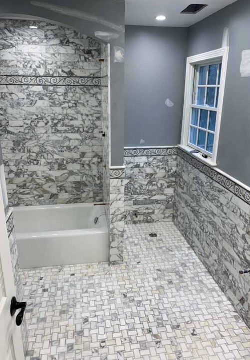 Marble looking ceramic tile wall with Victorian stencil pattern accent, a bathtub, and a basketweave tile flooring
